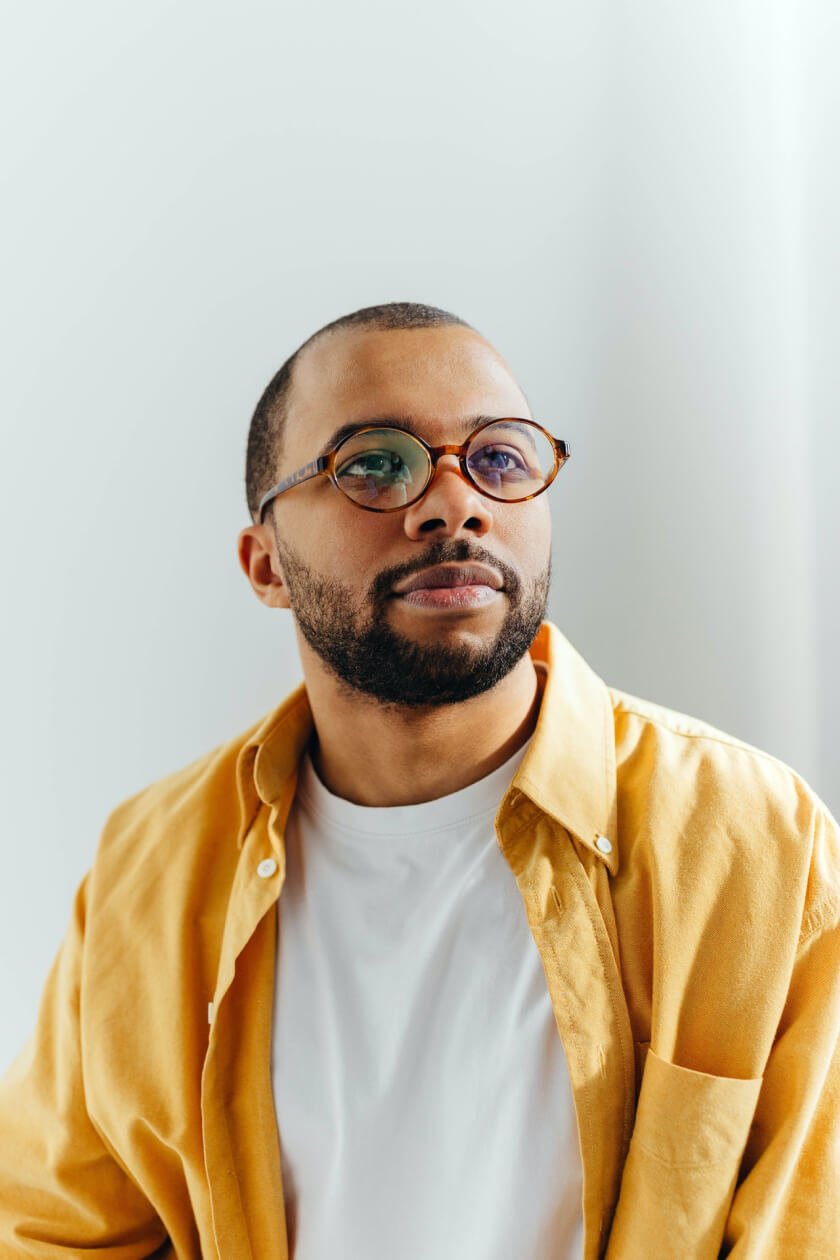 Bearded man with glasses wearing white t-shirt and yellow dress shirt looking off in the distance